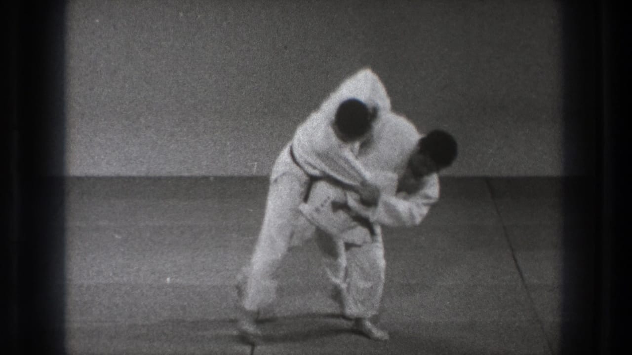 The throwing motion continues on the indoor mat, with one man bent forward and the other being lifted off balance.