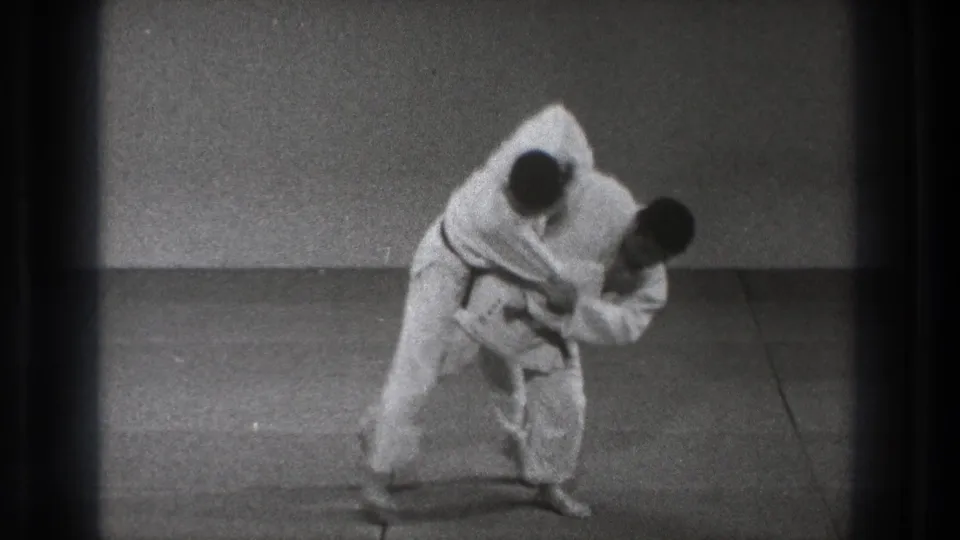 The throwing motion continues on the indoor mat, with one man bent forward and the other being lifted off balance.