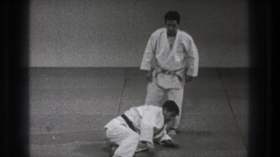 After the throw in the 1971 Tokyo martial arts footage, one man is down on hands and knees while his partner stands beside him.