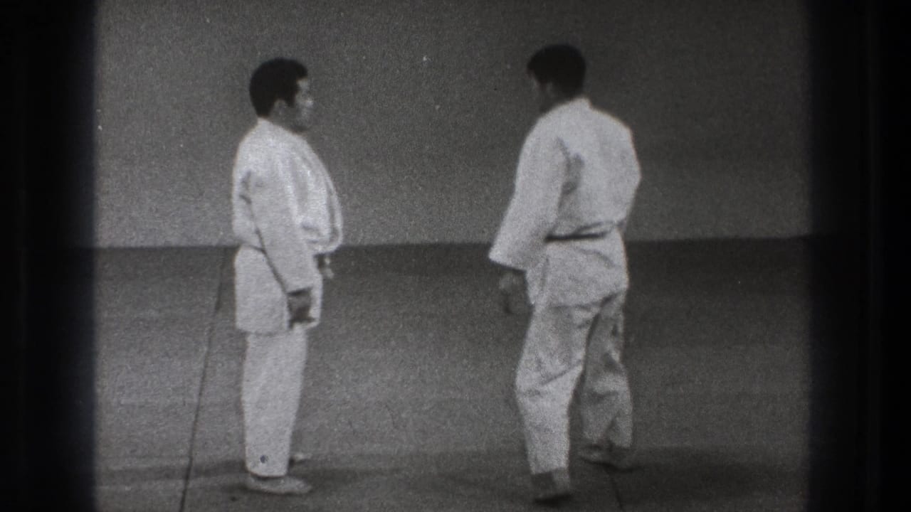 In the supported 1971 Tokyo clip, two adult men in white judo gis stand in a simple dojo-like mat space before practice.