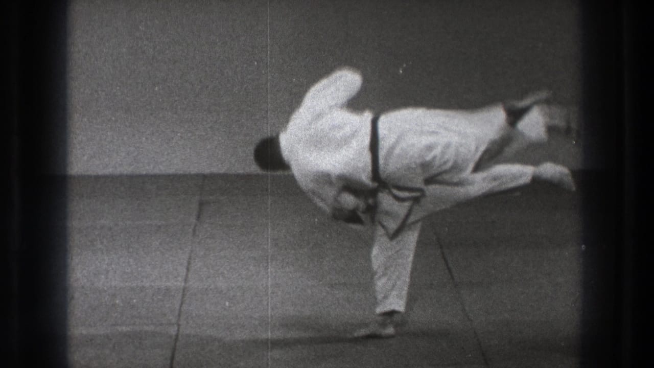 Two judo practitioners in white gi during a throw on an indoor mat.