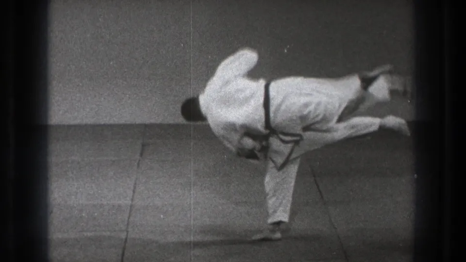 In 1971 Tokyo footage, one judo practitioner turns in close as the other is lifted sideways during a throw on a dojo mat.