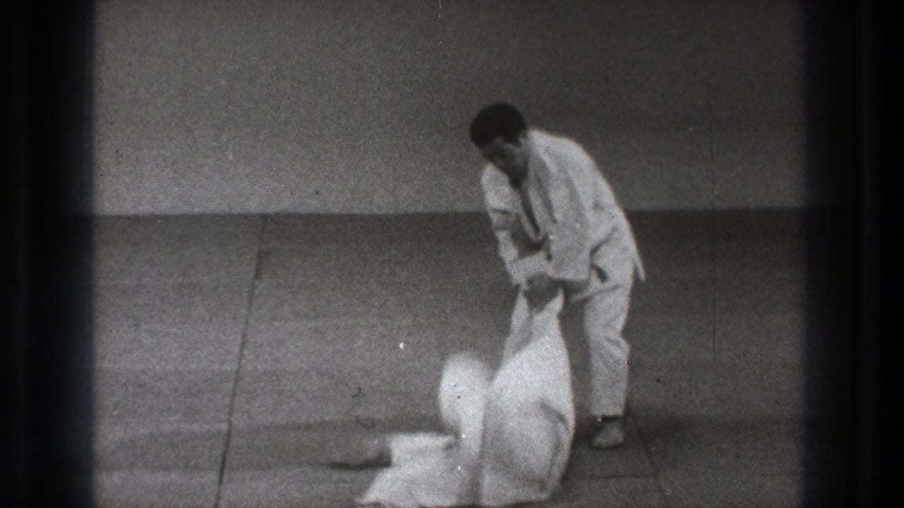 After the throw, one practitioner stands and holds the other by the gi as the opponent lies on the dojo mat.