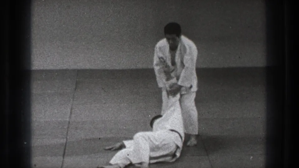 The 1971 Tokyo dojo scene ends with one practitioner standing over a partner on the mat after a completed judo throw.