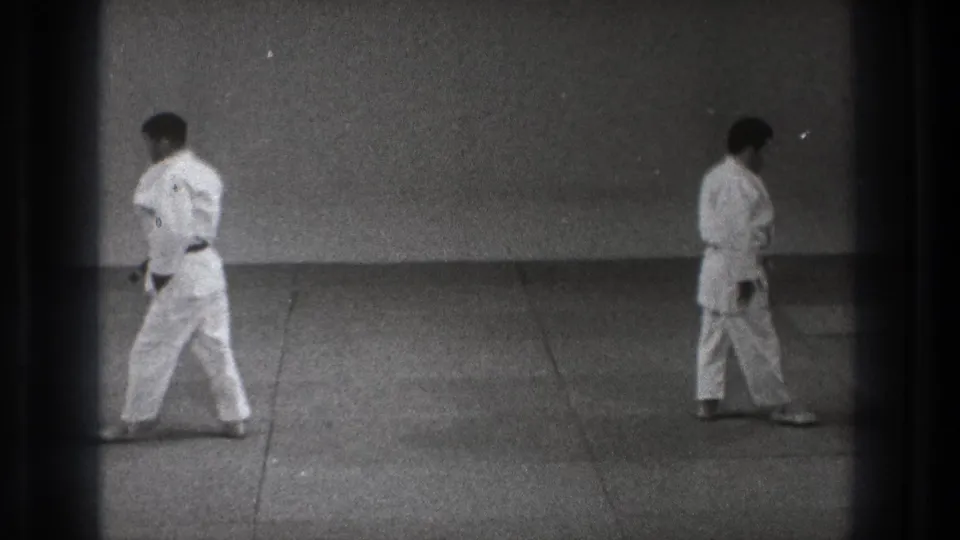 The clip ends with two men in judo uniforms moving apart across the tatami, framed in grainy black-and-white 8mm footage.