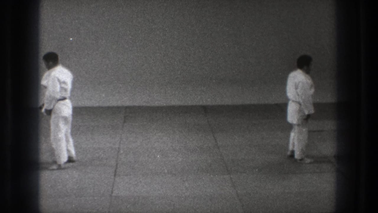 Two men in white martial arts uniforms stand apart on a mat floor.