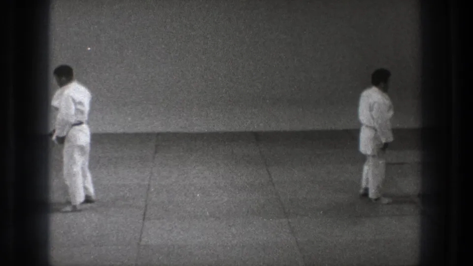 In 1971 Tokyo archival footage, two men in white gi stand at opposite sides of a mat-lined practice space.