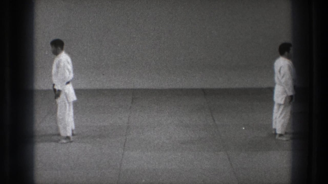 Two men in white martial arts uniforms stand apart on a tiled floor.