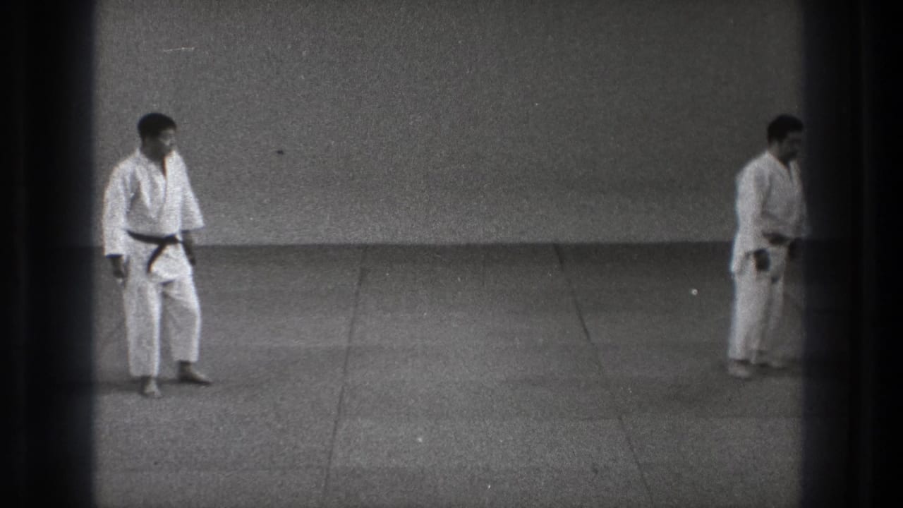 Two men in white martial arts uniforms face each other across a tiled floor in the supported Tokyo 1971 home-movie clip.