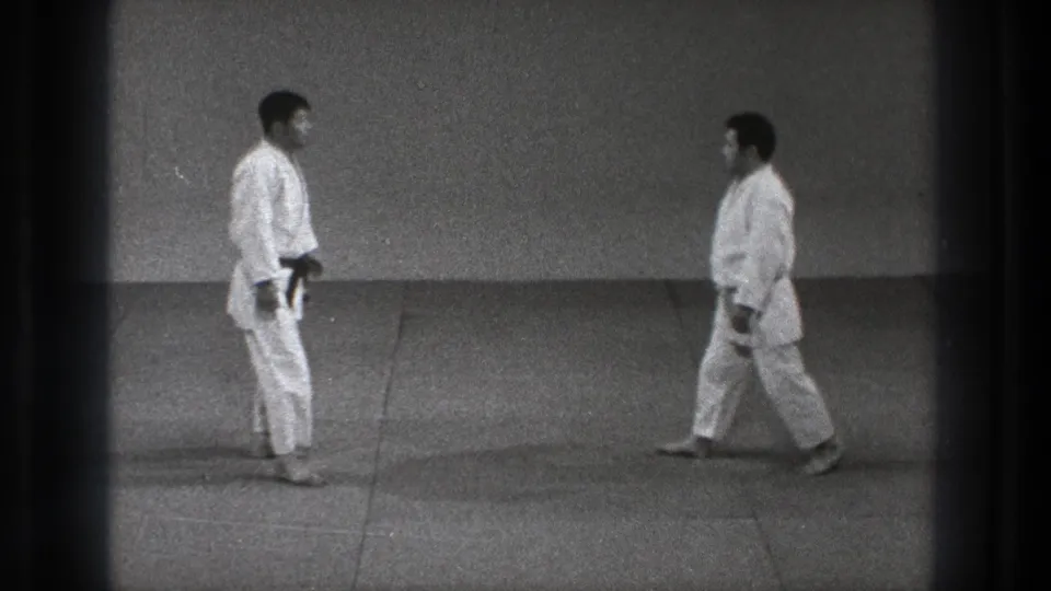In metadata-supported 1971 Tokyo footage, two adult men in gi face each other across a dojo mat before contact.