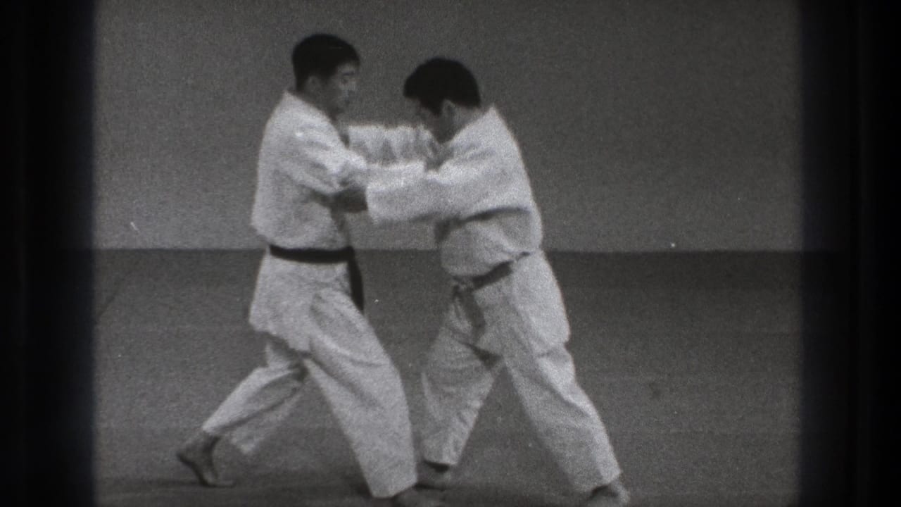 The two adult practitioners shift weight and lean into a close-range technique on the dojo mat in metadata-supported Tokyo footage.