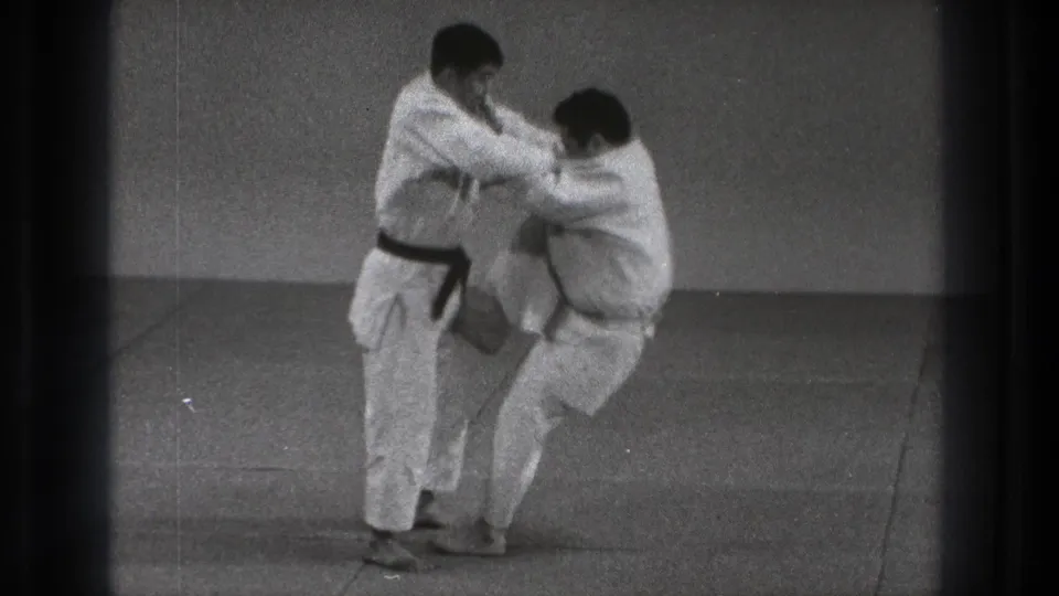 During the 1971 Tokyo practice, the black-belt practitioner lifts his partner from the mat as the body throw begins indoors.
