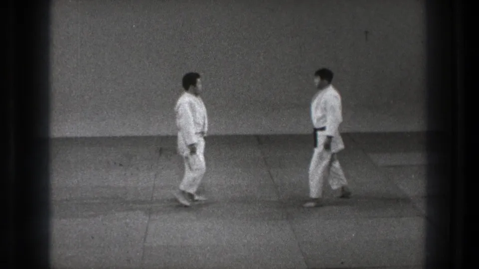 The practitioners move toward one another on the mat, framed by a bare wall and the soft grain of 1971 Tokyo 8mm footage.