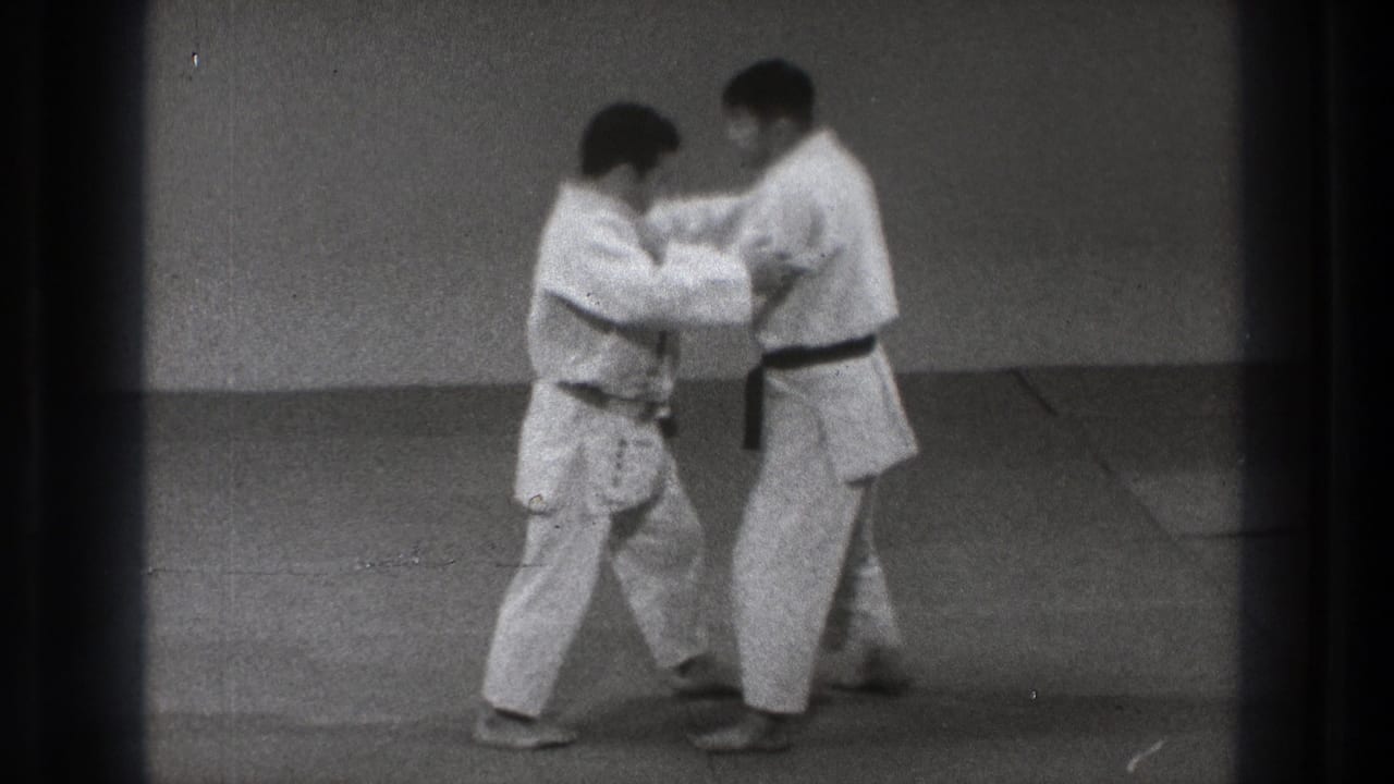 Two judo practitioners begin a controlled grip exchange on the mat in the supplied 1971 Tokyo home-movie clip.