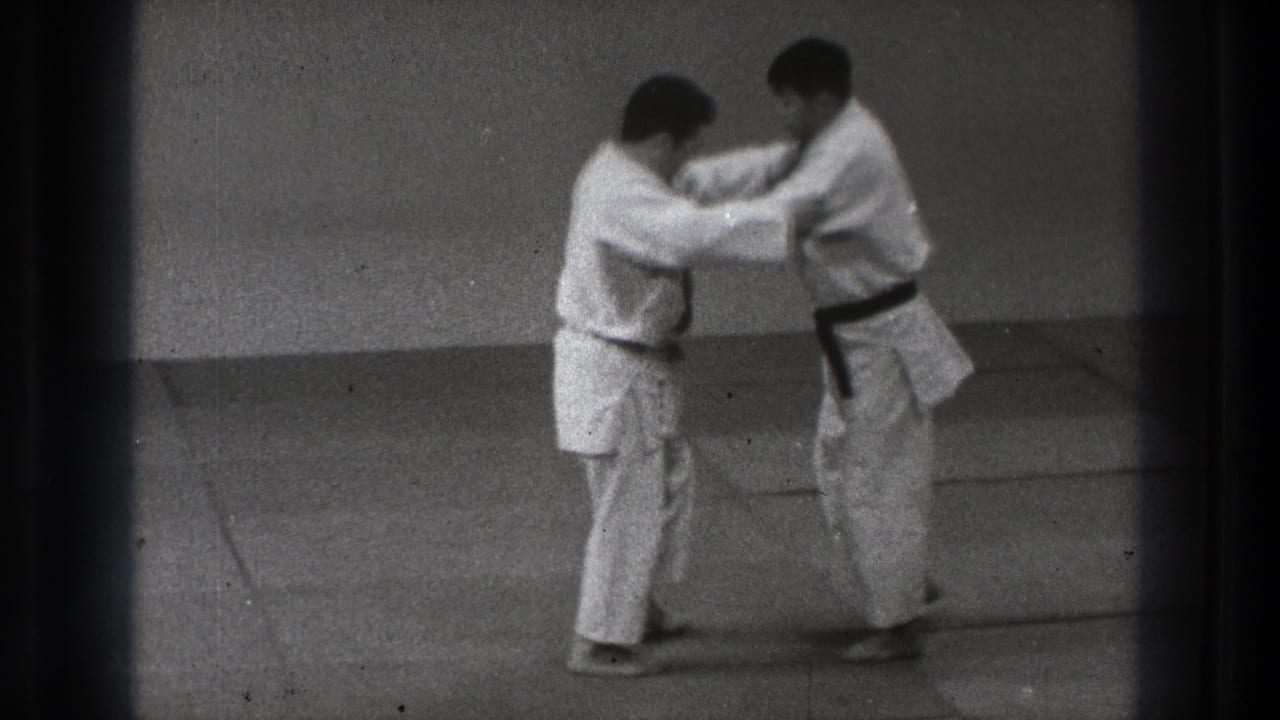 Two men in white judo uniforms hold grips as one steps back during a controlled technique demonstration.
