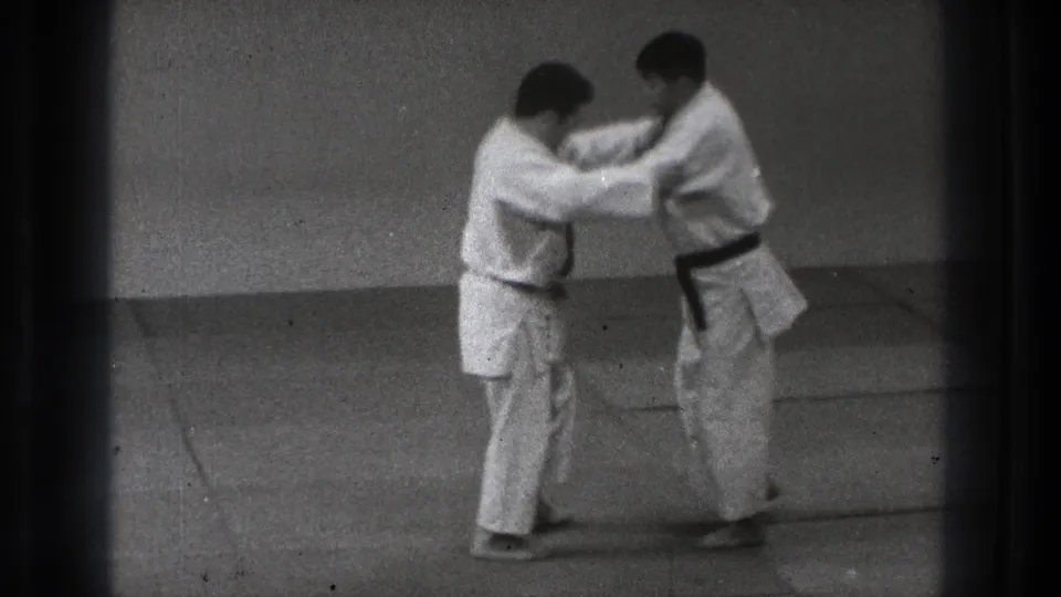 Two men in white judo uniforms hold grips as one steps back during a controlled technique demonstration.