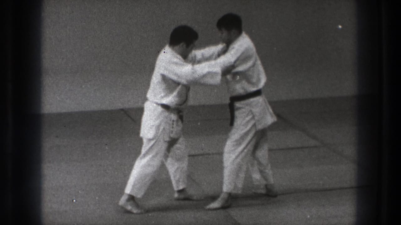 Two men in white martial arts uniforms grip each other on a mat.