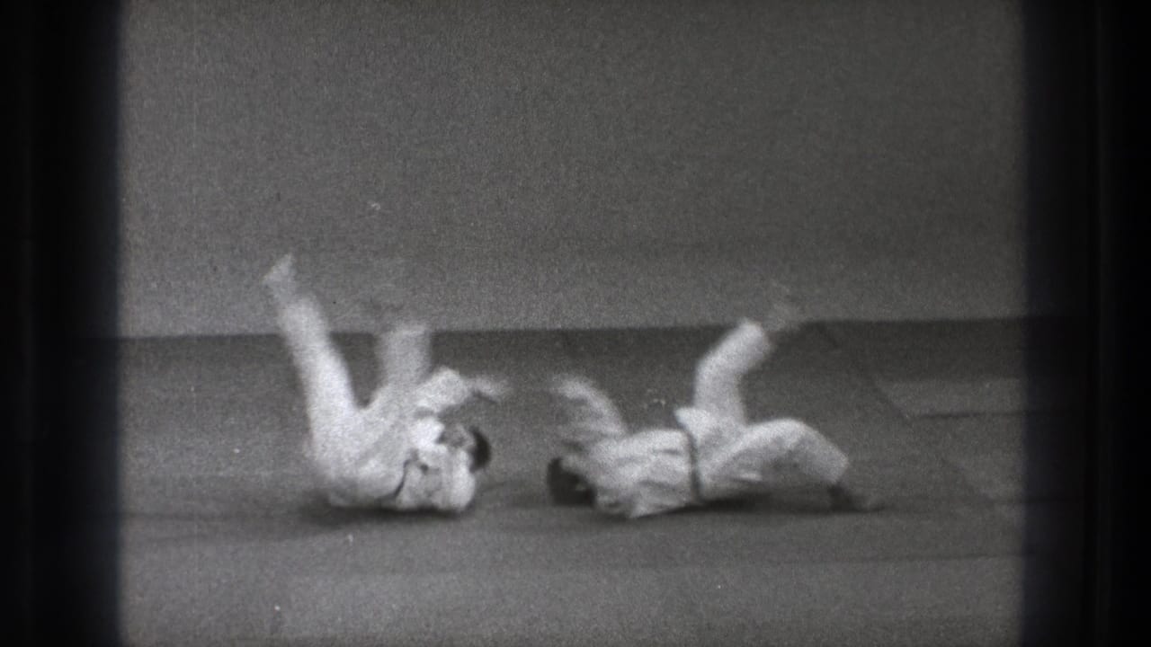 Two adult practitioners in white gi land on the mat during a judo-style throw in black-and-white 1971 Tokyo footage.