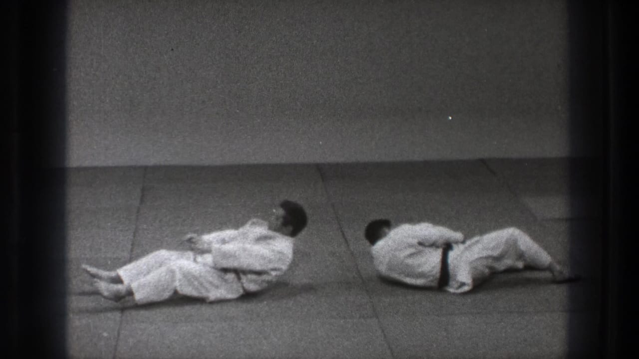 1971 Tokyo 8mm frame showing two martial artists in white gi on the mat after a judo throw or fall.
