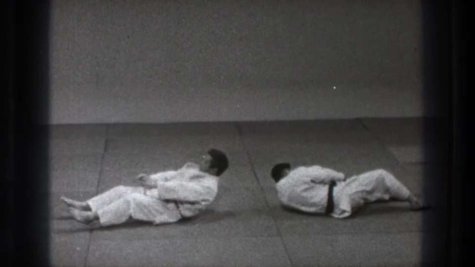 1971 Tokyo 8mm frame showing two martial artists in white gi on the mat after a judo throw or fall.