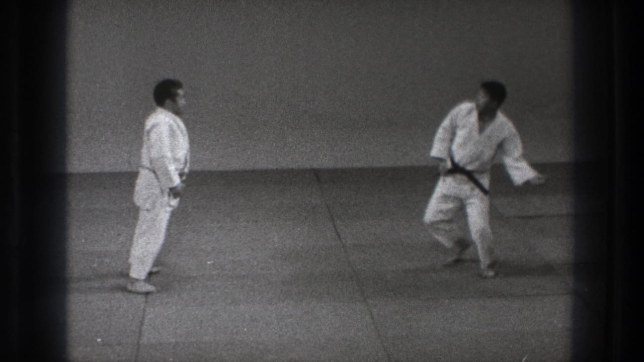 1971 Tokyo 8mm frame showing two martial artists in a dojo-like mat room, one standing while the other steps away.
