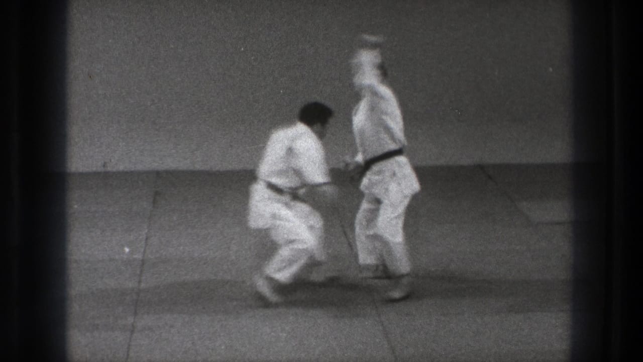 Two martial artists in white gi begin a standing grappling move on a mat.