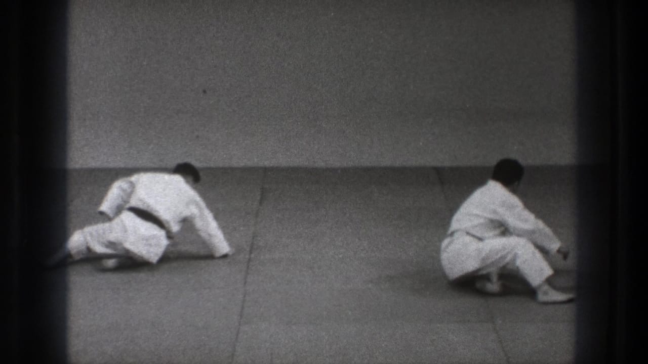 At the end of the Tokyo 1971 judo sequence, both practitioners reset on the mat, one pushing up while the other sits or kneels nearby.