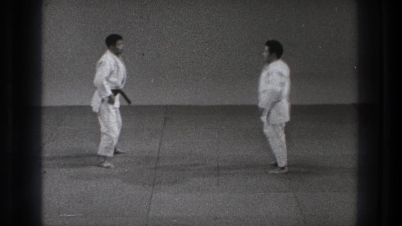 Two karate practitioners in white gi face one another in a simple indoor dojo setting in 1971 Tokyo footage.