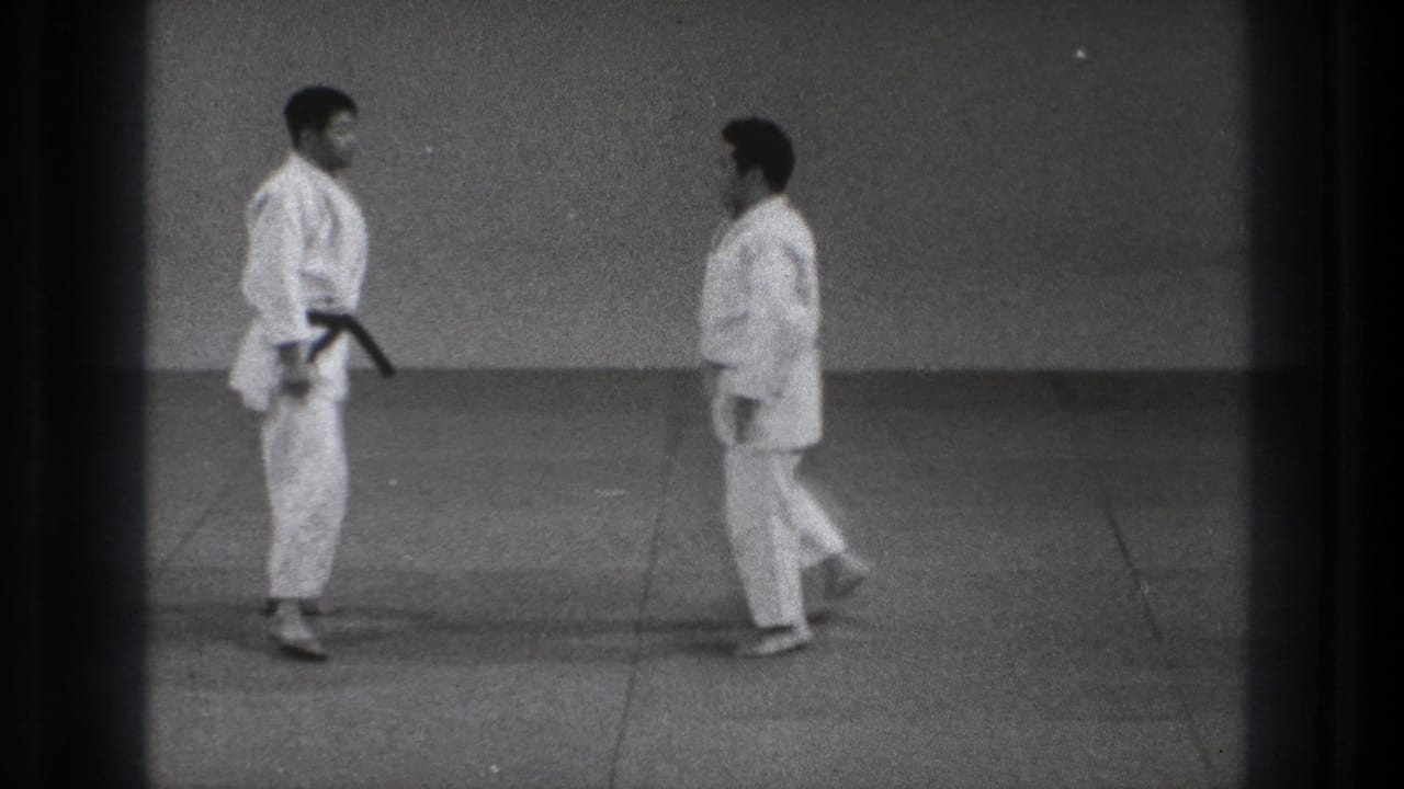 Two men in white karate uniforms walk toward one another on a tatami-style mat in archival Tokyo footage.