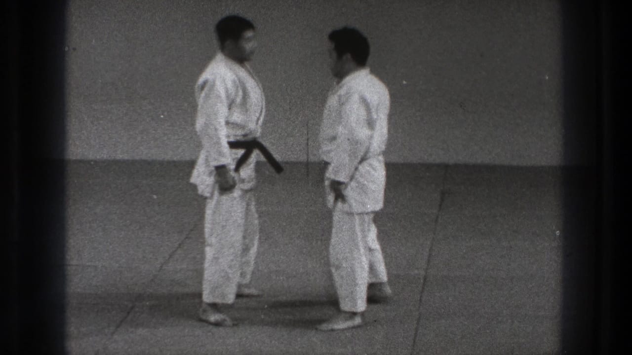Two men in karate gi stand face to face at close range in a plain indoor practice space, Tokyo, 1971.