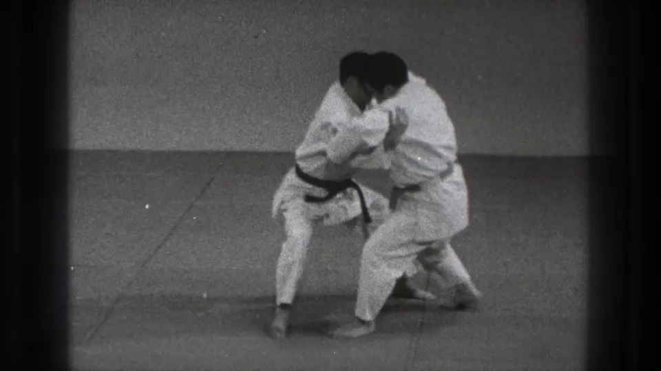 The practitioners stay low while gripping each other, suggesting the middle phase of a throw or takedown demonstration.