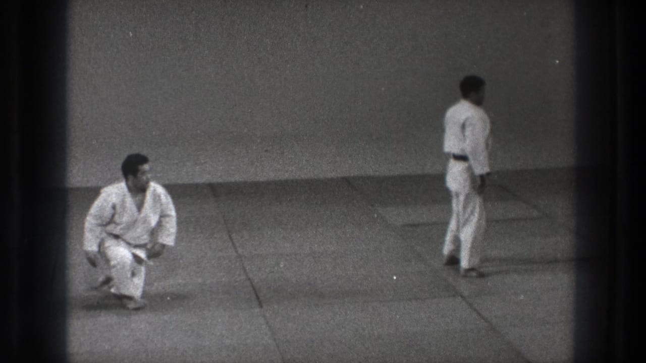 One martial artist kneels and looks toward his standing partner during the reset of the 1971 Tokyo self-defense demonstration.