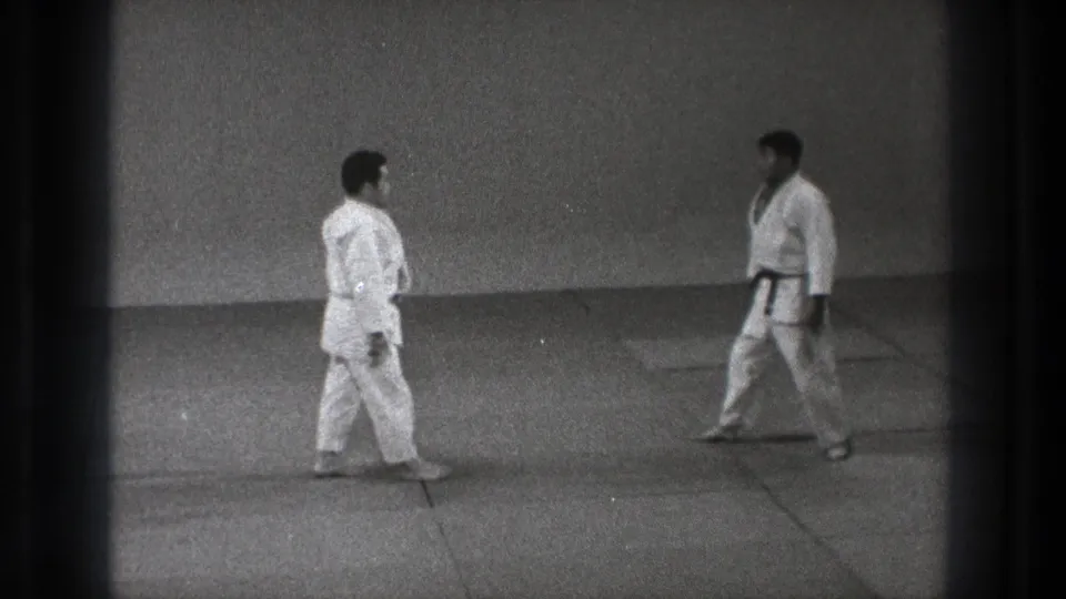 In the supplied 1971 Tokyo clip, two adult judo practitioners in white gi walk toward each other on tatami mats.