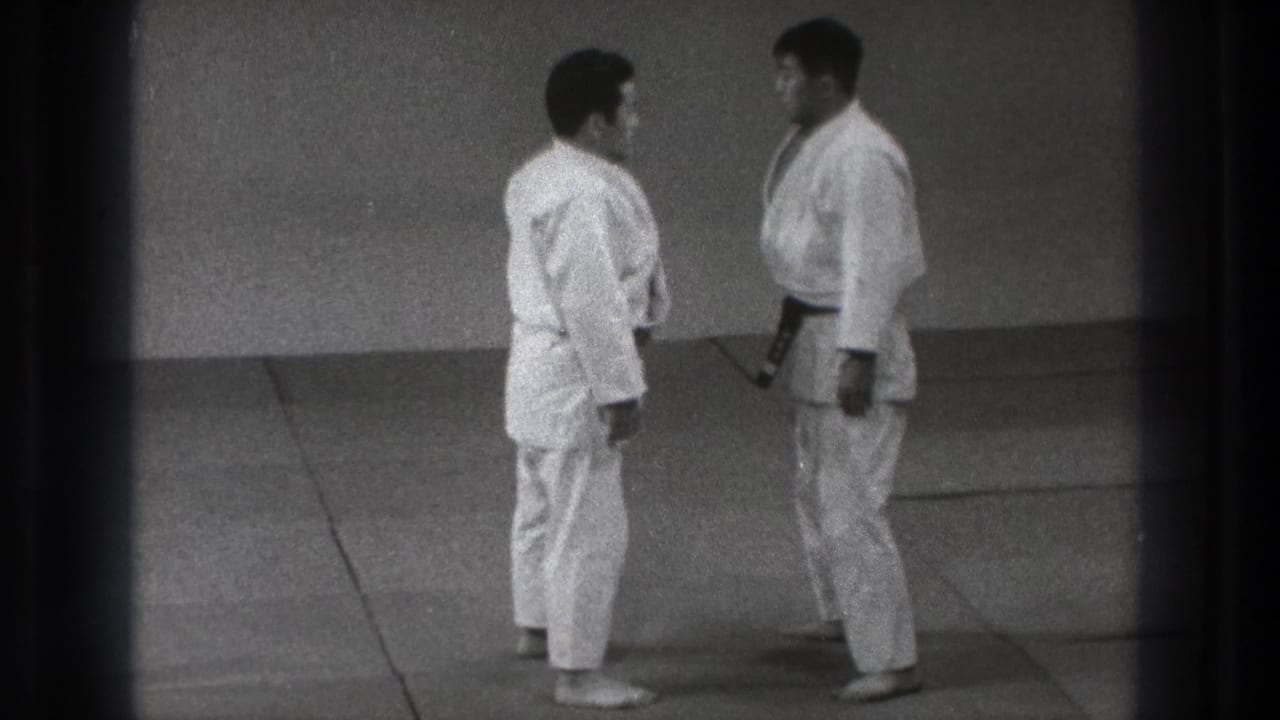 The two practitioners pause almost chest to chest, with one dark belt visible against the white gi.