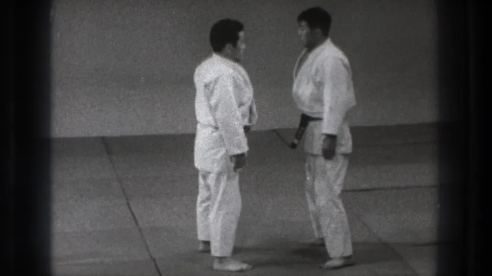 The two practitioners pause almost chest to chest, with one dark belt visible against the white gi.
