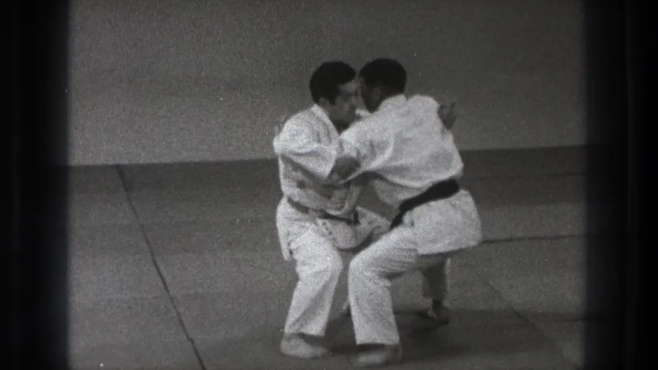 The Tokyo judo footage shows two adult practitioners gripping each other in a low, controlled grappling position.