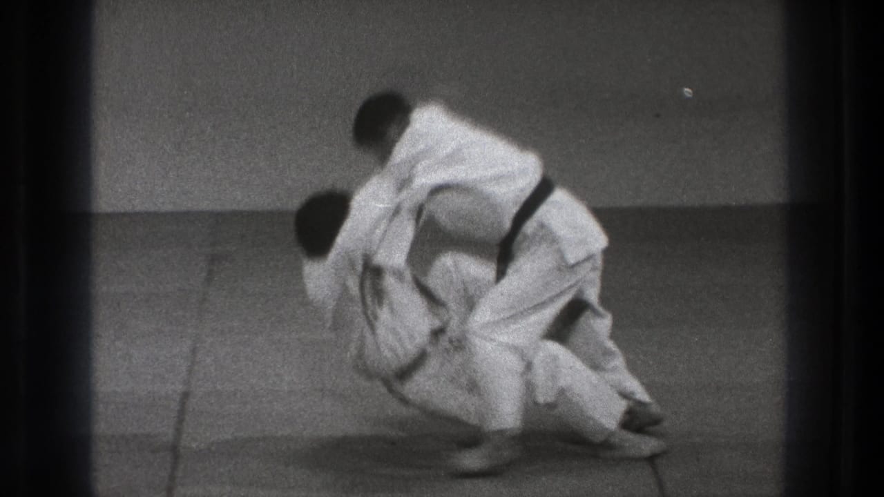 A judo throw is underway as one practitioner turns through the grip and the other loses balance over the tatami in the 1971 Tokyo clip.