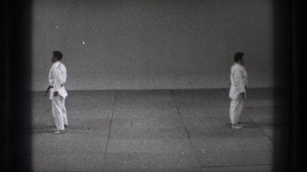 Two martial artists in white gi stand separated in a formal stance, with visible 8mm frame edges and grain.