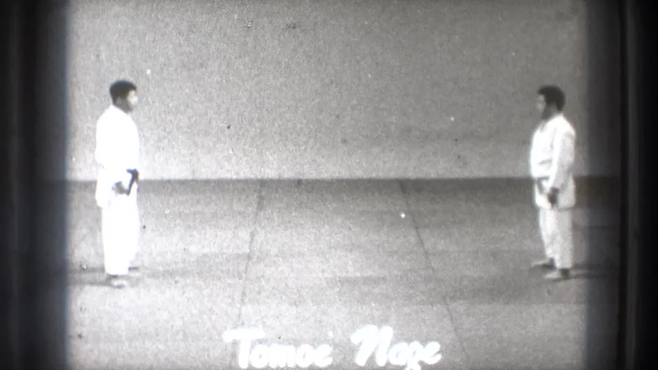 1971 Tokyo 8mm frame showing two martial arts practitioners in white gi facing each other on a plain mat, with Tomoe Nage text visible.