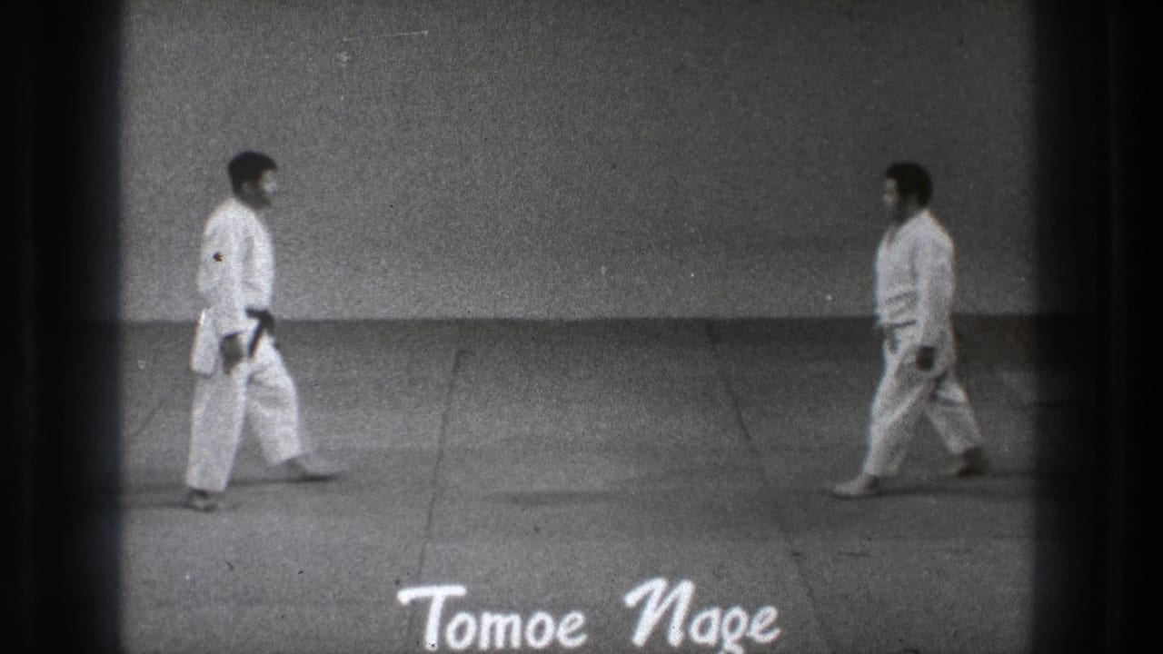 1971 Tokyo martial arts demonstration frame with two practitioners walking toward each other on a mat, seen in grainy 8mm footage.