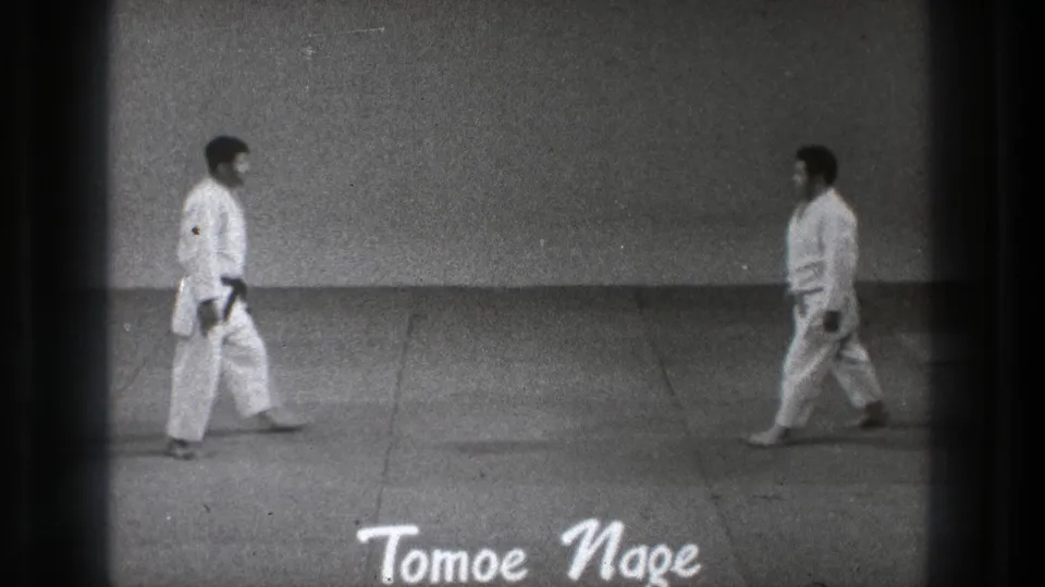 1971 Tokyo martial arts demonstration frame with two practitioners walking toward each other on a mat, seen in grainy 8mm footage.