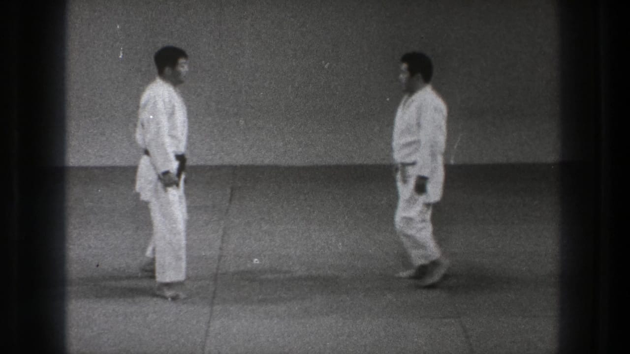 1971 Tokyo 8mm frame showing two martial arts practitioners nearing a face-to-face stance on a plain training mat.
