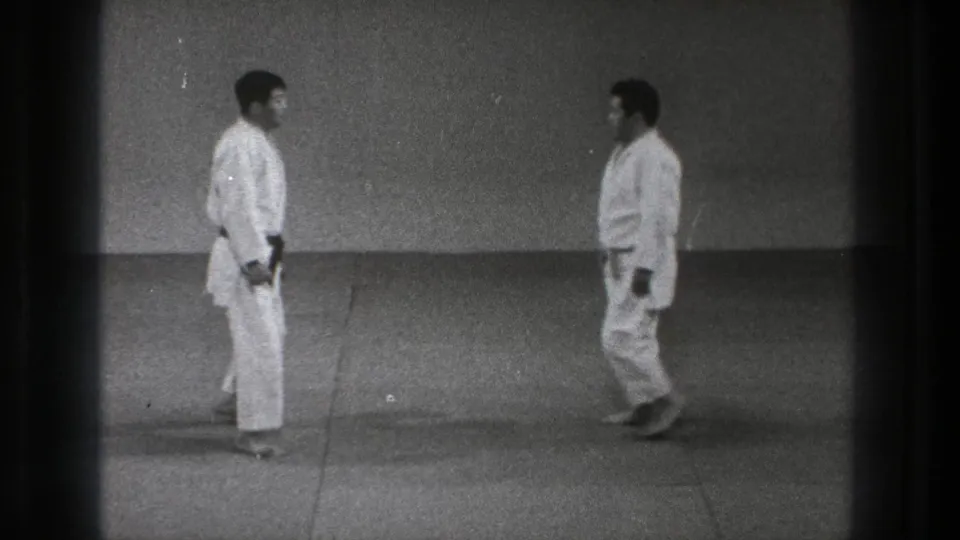1971 Tokyo 8mm frame showing two martial arts practitioners nearing a face-to-face stance on a plain training mat.