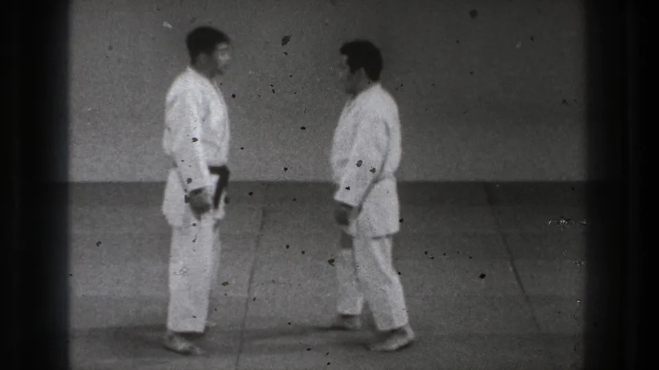 1971 Tokyo 8mm frame with two practitioners standing face to face in white gi during a Tomoe Nage demonstration setup.