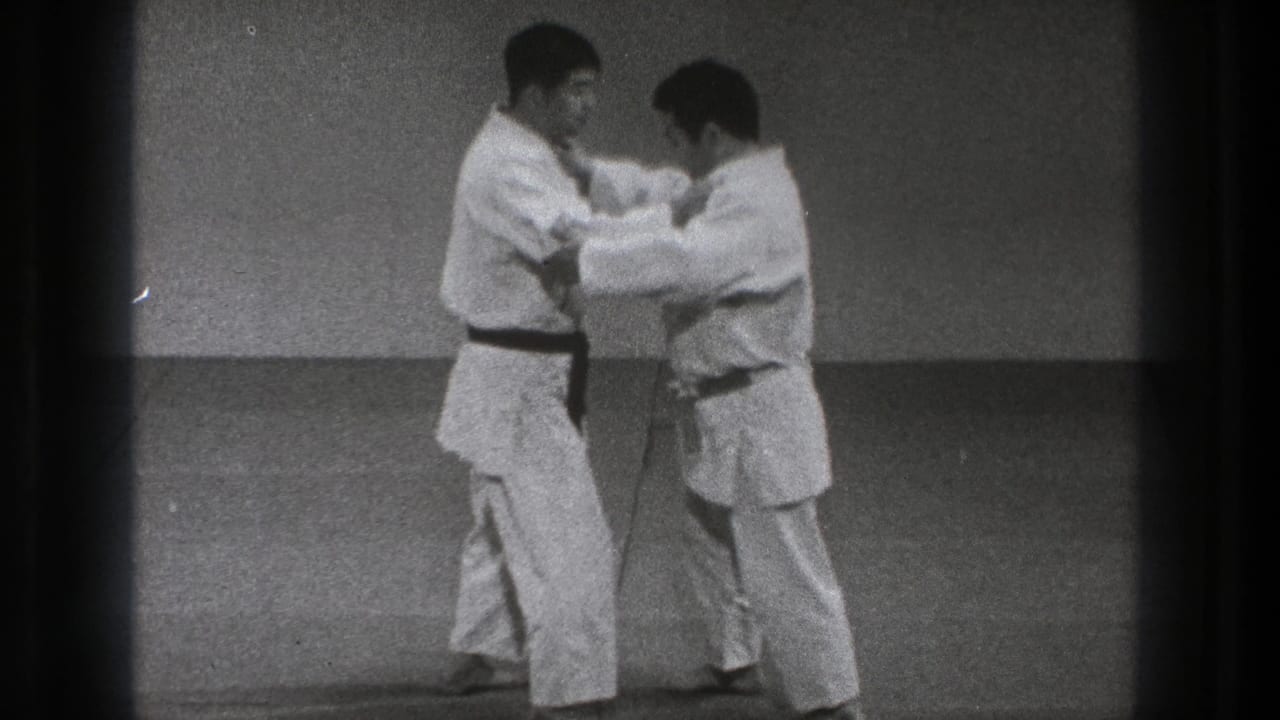 Two martial artists make upper-body contact while standing on a mat.