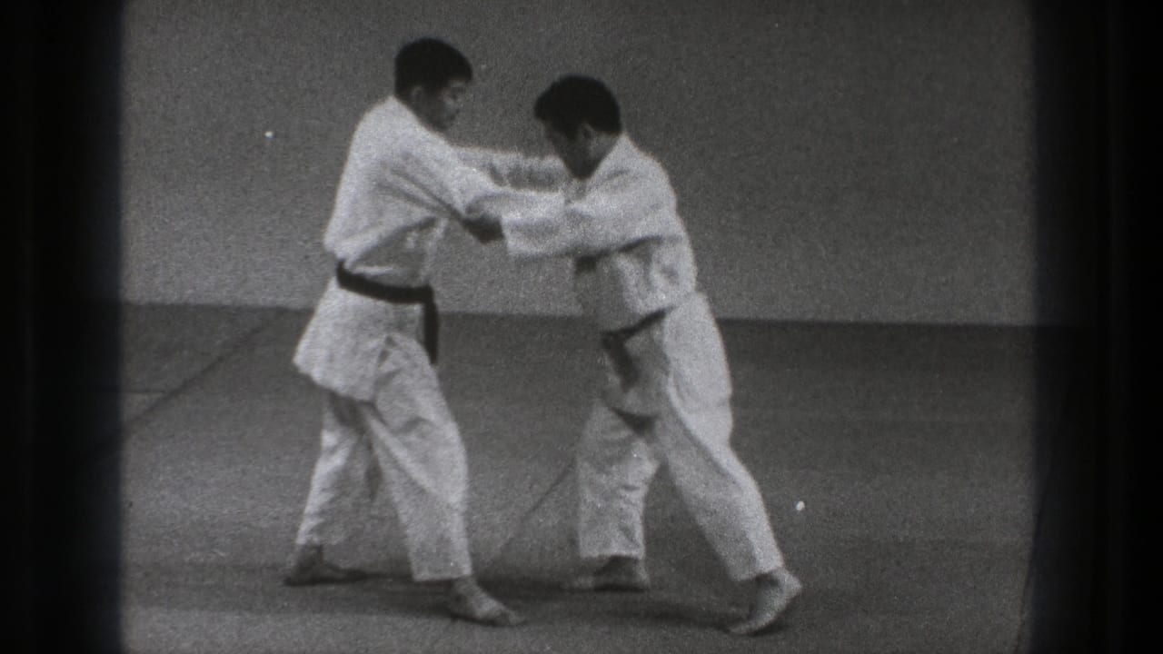 Two adult martial artists in 1971 Tokyo footage lean into a close grip with bent knees and braced footing on the mat.