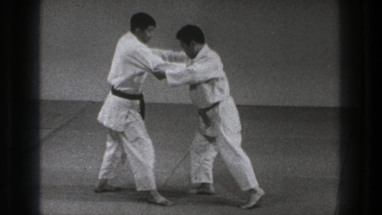 Two men in white gi grip each other on a mat during a martial arts demonstration.