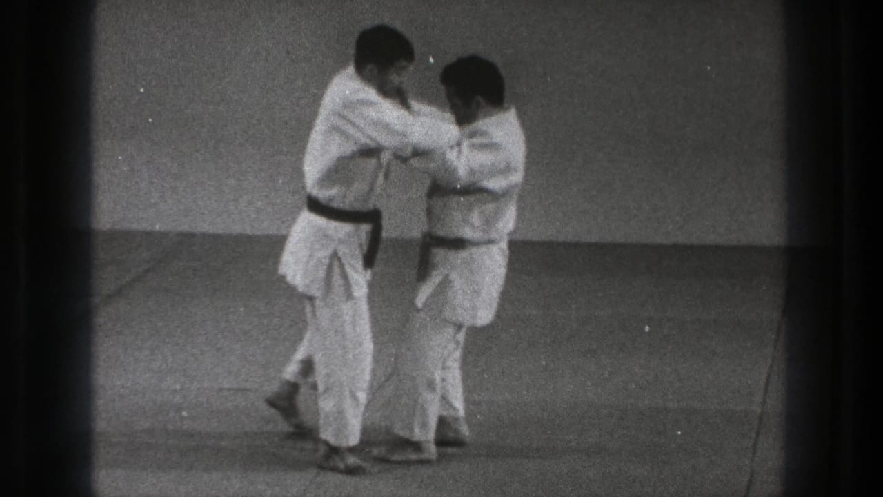 In Tokyo, Japan in 1971, two adult men in white gi and dark belts grip each other at the start of a martial arts throw demonstration.