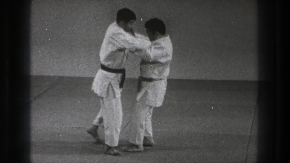In Tokyo, Japan in 1971, two adult men in white gi and dark belts grip each other at the start of a martial arts throw demonstration.