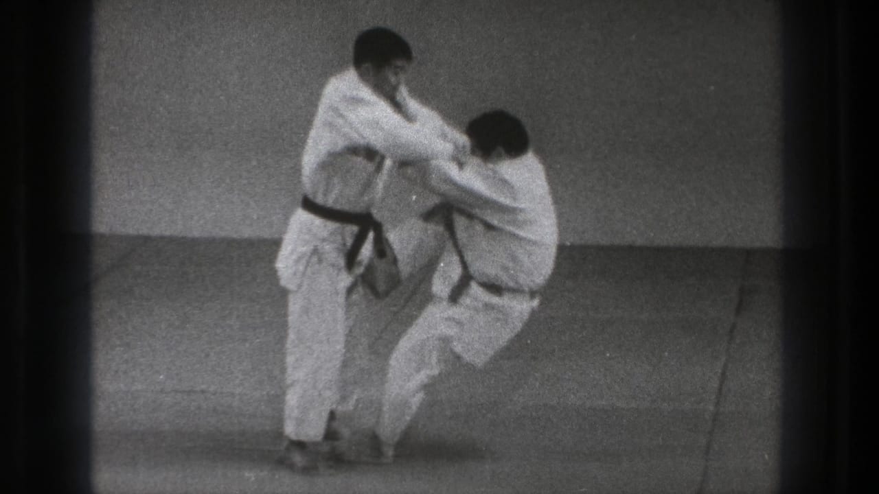 The black-belt practitioner begins the throw, drawing his partner off balance on a plain indoor mat in 1971 Tokyo footage.